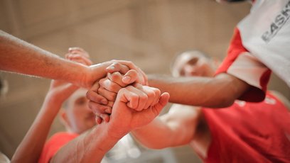 Zu sehen ist eine Gruppe von Menschen, die ihre Hände für einen Teamspruch im Kreis stehend zusammenführen.